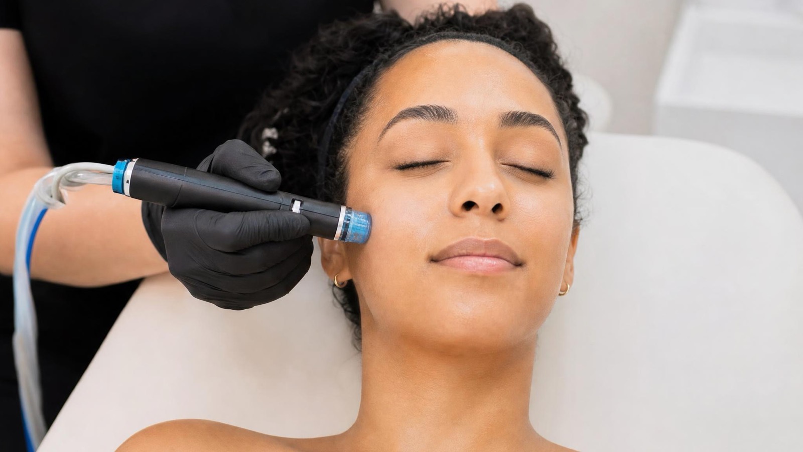 Gloved practitioner glides a HydraFacial® wand across a relaxed client's cheek
