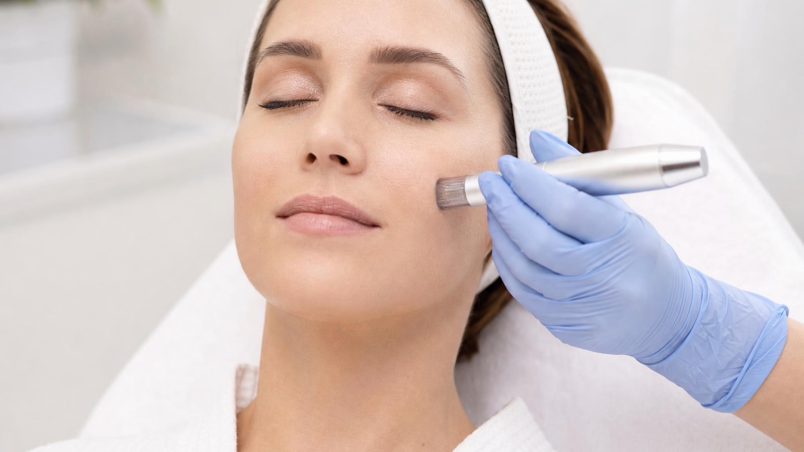 Gloved practitioner guides a microneedling pen across a relaxed client's cheek